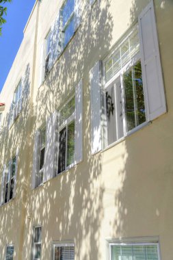 San Francisco, Kaliforniya 'da bej rengi dış görünüşlü bir binanın alçak açılı görüntüsü. Evin dış tarafında ağaçların gölgeleri ve camlarında sahte panjur tasarımları var..