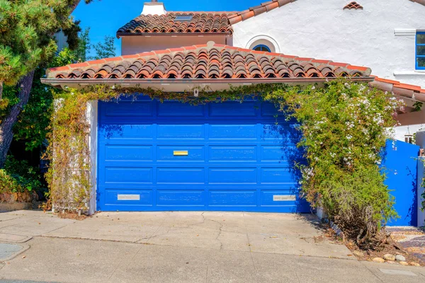 Garage of a mediterranean house with blue sectional garage door and gate in San Francisco, CA. Front exterior of a house with vines at the side of the garage door and concrete driveway.