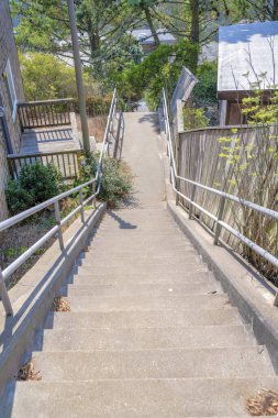 Metal tırabzanlı beton merdivenler ve San Francisco, California 'ya iniş. Evin ortasındaki yüksek açılı merdiven manzaralı arka taraftaki ağaçlara çitlerle ve bitkilerle çevrili..