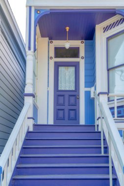 San Francisco, California 'da beyaz bukleli ve parmaklıklı bir evin mor girişi. Mor kapı basamakları ve cam panelli ön kapısı olan bir evin verandası..