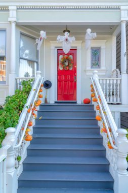San Francisco, Kaliforniya 'da cadılar bayramı süsleri olan bir evin merdivenleri. Verandanın önündeki korkuluklarda balkabakları var. Kırmızı kapının yanında çelenkli hayaletler asılı..