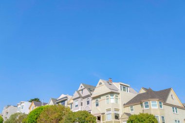 San Francisco, California 'da çatısı olan evleri alçak açılı görüyor. İki katlı evlerin önünde açık mavi gökyüzü arka planına karşı ağaçlar var..