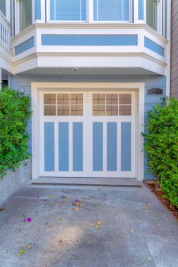 Açık mavi paleti ve beyaz süslemeleri olan garaj dışı San Francisco, California 'da. Çalıların ortasında beton bir garaj kapısı ve cam paneli var..