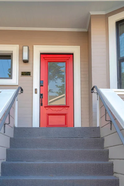 Red front door with window panel and digital key lock at San Francisco, California. There is a stairs with gray steps and metal railings at the front leading to the front door with modern wall lamp.