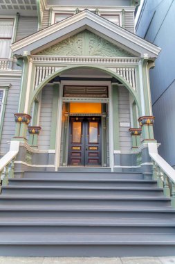Entrance exterior of a victorian house with gray doorsteps at San Francisco, California. Porch with arched colums with ornate trims and a view of double door and large transom window. clipart