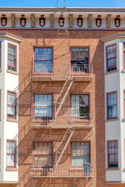 Emergency stairs outside an industrial apartment building at San Francisco, California. Residential building with bricks wall cladding in the middle of white bay windows exterior on the side.