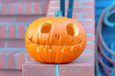 San Francisco, CA binasının dışında gözü, burnu ve ağzı oyulmuş bir balkabağı. Yarım duvar tuğlalarının üstünde balkabağı dekoru..