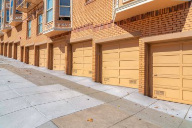 San Francisco, CA 'da sarı turuncu tuğlalı duvarları olan bir apartmanın garaj kapıları. Beton yollu eğimli bir arazide konut binası..