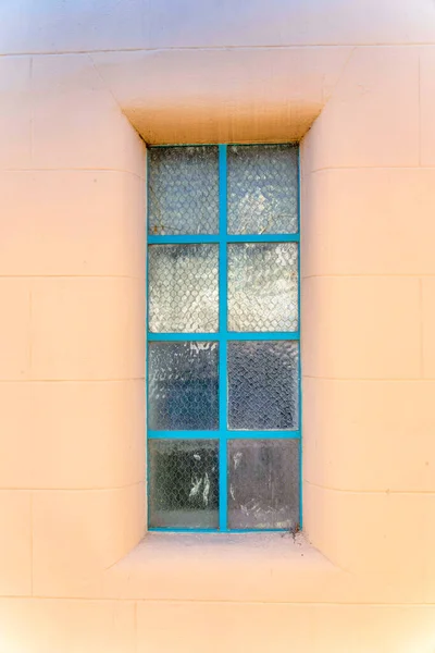 Window with frosted glass panes at San Francisco, California. Close-up of a window with sky blue grids in the middle of a painted concrete building wall.