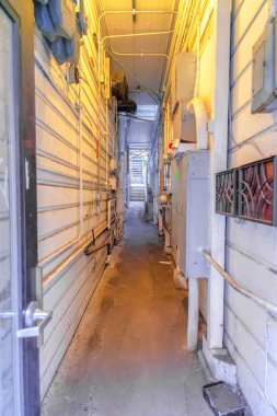 San Francisco, California 'daki iki konut arasında dar bir yol var. Sağda cam bir kapı ve iki tarafında borular ve kablolar olan iki beyaz duvar var..