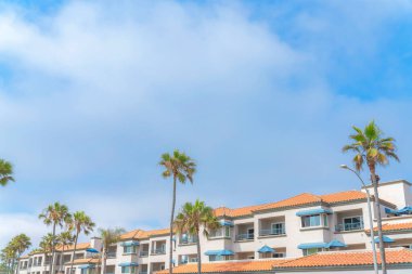 Carlsbad, San Diego, California 'da beton kiremitli çatıları olan kompleks bir binanın dışı. Gökyüzü arka planına karşı mavi pencere güneşlikleri ve parmaklıkları olan bir binanın düşük açılı görüntüsü.