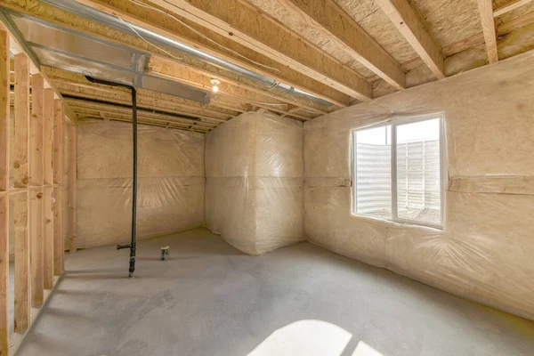 Penceresi pencereli, tamamlanmamış bir bodrum katı. Solunda siyah metal boru ve ahşap çerçeveli bodrum katı..