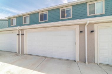 Birinci katta beyaz garaj kapısı olan kasaba evlerinin dışında. Bölümsel kapıları ve duvar lambaları arasında su boruları olan garaj ve ikinci katın dış görünüşü vinil kaplamalı..