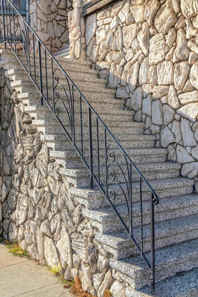 Outdoor staircase with granite steps and wrought iron railings at San Francisco, California. Staircase with gray stone veneer walls and landing.