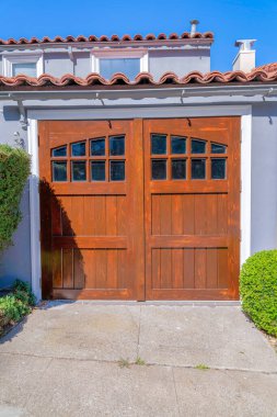 San Francisco, Kaliforniya 'da cam pencere panelleri olan yan menteşeli ahşap garaj kapısı. Yanlarında çalılar olan beton bir garaj yolu ve beyaz duvarlı ve beton çatılı bir ev manzarası..