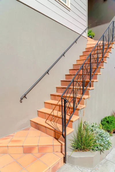 Outdoor staircase with tiled steps and iron railings at San Francisco, California. Entrance of a house with gray exterior and plants near the wall of the stairs.