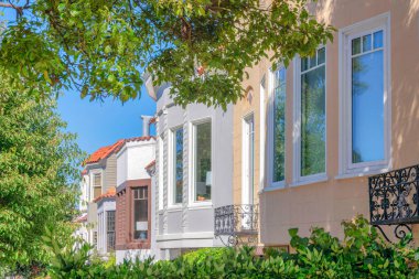 San Francisco, California 'da penceresi olan kompleks evler. Konut binalarının önünde açık mavi gökyüzü arka planına sahip taze yeşil yapraklı çalılar ve ağaçlar var..