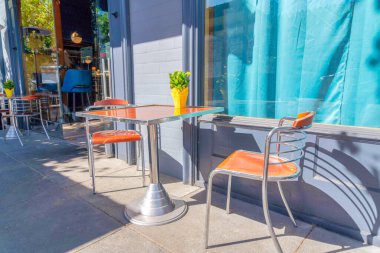 San Francisco, California 'daki restoranın dışındaki yemek masasında. Yan tarafta iki sandalyeli yemek masaları. Mor duvarları ve cam pencereleri olan binanın dışında yürüyorlar..