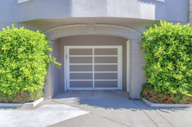 Ön tarafı San Francisco, California 'da kemerli girişi ve kırpılmış çalıları olan bir garaj. Beyaz şebeke ve beton yolu olan gri bir garaj kapısı var..