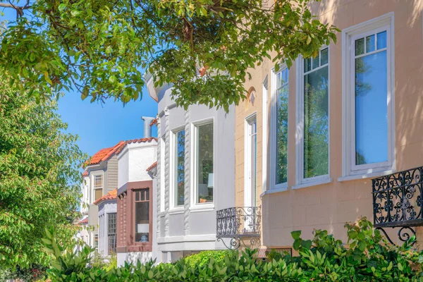 San Francisco, California 'da penceresi olan kompleks evler. Konut binalarının önünde açık mavi gökyüzü arka planına sahip taze yeşil yapraklı çalılar ve ağaçlar var..