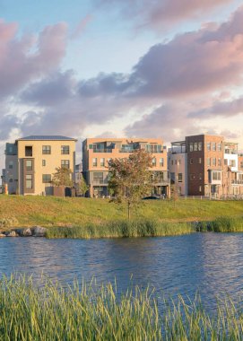 Günbatımında, Utah, Daybreak 'teki yerleşim merkezinin önündeki Oquirrh Gölü' nde dikey kabarık bulutlar. Yansıtıcı göl kıyısı, kıyıda otlar, solda kemer köprüsü ve arkada dağların manzarası..