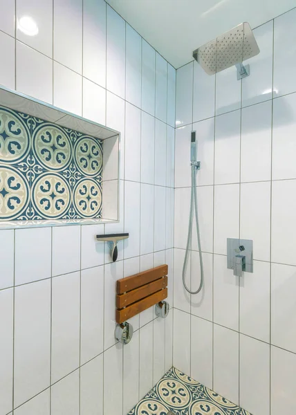 Vertical Shower stall interior with white ceramic tiles surround and cement tiles with blue patterns. There are wall mounted and handheld shower heads near the adjustable soap dish on the right.