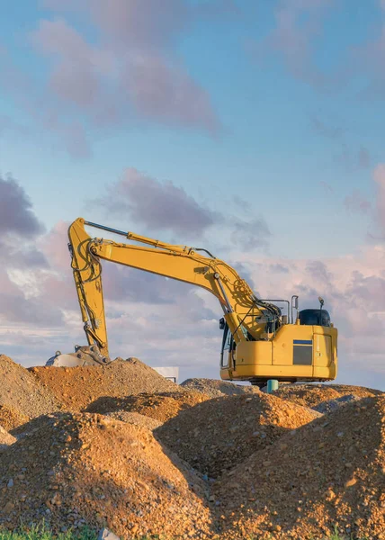 Vertical Puffy clouds at sunset Rocky sand piles with yellow excavator on top at Utah. Piles of construction sands outside the unfinished house on the left with cork wall insulation against the clouds on the sky.