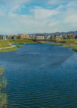 Utah 'ta Şafak vakti, üzerinde asfalt kaldırım olan dikey Whispy beyaz bulutları Oquirrh Gölü. Gölün üzerinde bir köprü ve arka planda dağlara karşı farklı yapılara sahip evler var..