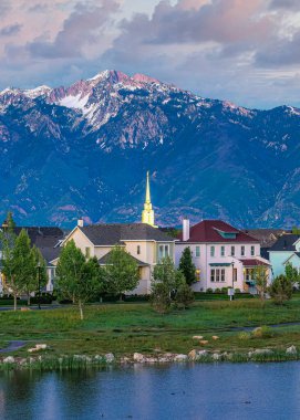 Günbatımında Oquirrh Gölü 'ndeki dikey kabarık bulutlar Daybreak, Utah' taki alacakaranlık gökyüzünün yansıması. Arka plandaki dağın manzarasına karşı asfalt yolda arabaları olan bir ev ve kilise manzarası var..