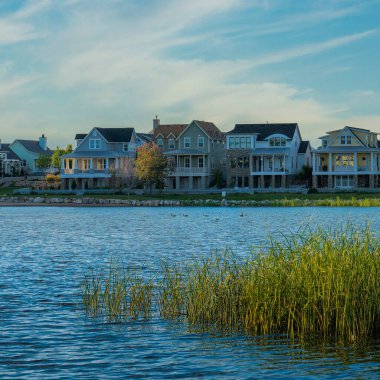 Kare Whispy beyaz bulutları Oquirrh Gölü kıyısı Daybreak, Utah 'ta gün batımında. Sol tarafta kapalı bir rıhtım ve arka planda gökyüzü ufkuna ve dağa karşı büyük evler var..