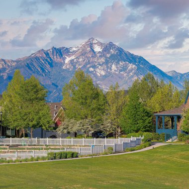 Gün batımında Kare Kabarık Bulutlar. Utah, Daybreak 'teki evlerin önündeki geniş bir tarlanın panoramik manzarası. Ağaçların güzel ve rahatlatıcı bir manzarası var. Arka planda dağlara karşı evler var..