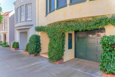 San Francisco, California 'daki garajın önünde asmalı evler var. Sağda açık sarı dış ve yeşil garaj kapısı ile başlayan kıvrımlı duvarları olan kasaba evleri..