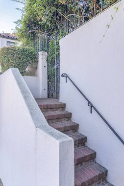 San Francisco, Kaliforniya 'da bir evin bej duvarında metal parmaklıklar olan tuğla merdivenler. Asma ve bitkilerle işlenmiş siyah işlemeli demir kapılı bir mülke giriş..