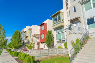 Complex multi-storey residential buildings with stairs at the front entrance at Daybreak, Utah. There is a concrete sidewalk on the left with columnar plants at the front of the buildings.