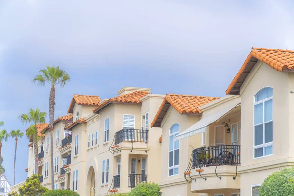 Complex apartment buildings with decorated balconies at Carlsbad, San Diego, California. There are palm trees and plants at the front of the buildings with concrete tile roofs.