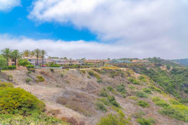 Laguna Niguel community on top of a mountain in Southern California. There are houses with glass fence near the edge of the mountain slope with shrubs and bushes.