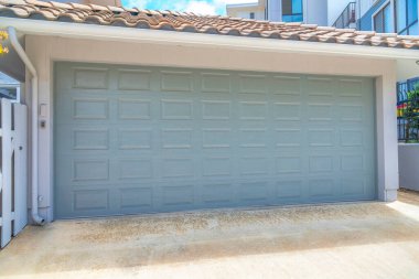Garage exterior with light gray sectional door at La Jolla in San Diego, California. Detached garage with water pipe on the left side.