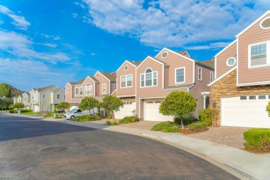 Townhouses with attached garage at Carlsbad, San Diego, California. There is an asphalt road pavement on the left and townhouses with pink and green exterior on the right.