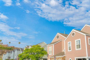 Townhouse complex buildings with gray and pink vinyl wood sidings at Southern California. Townhouses with trees outside near the hill with bushes and houses on top.