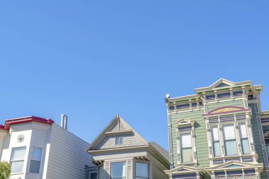 Low angle view of houses with different designs against the clear sky in San Francisco, California. There is a house on the right with green exterior beside the house in the middle with gable roof.