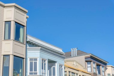 Residential buildings in a low angle view with different designs and exterior in San Francisco, CA. View of top part of neighborhood against the clear blue sky.