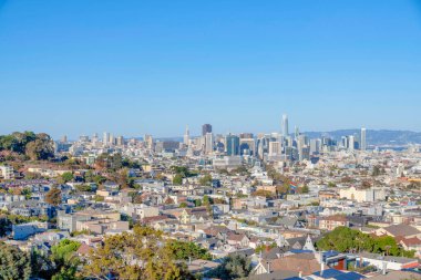 San Francisco downtown in California against the clear blue sky background. There are houses and streets at the front and a view of skycrapers at the back.