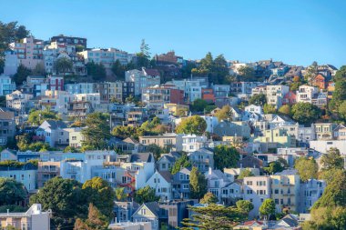 Residential buildings on a sloped neighborhood in San Francisco, California. Rows of residences with trees outside and a view of clear blue sky.