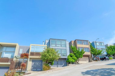 Modern complex houses buildings on a sloped neighborhood in San Francisco, California. Residential buildings with picture windows and garage doors with trees at the front.