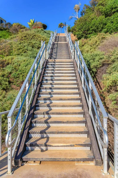 Outdoor stairs with wooden steps and metal railings at San Clemente, California. Stairs on a slope of a mountain against the clear sky.