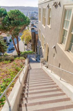 High angle view of a staircase outside a building with a view of the neighborhood at the background. Outdoor stairs with handrail near the beige wall of a building on the left in San Francisco, CA.