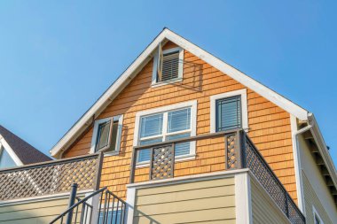 Low angle view of a house with wood shingles wall sidings and side hinged windows. Home exterior with wooden railings on the veranda and metal handrails on the stairs at the front.