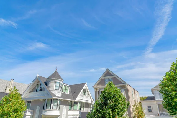 Single-family homes with gray walls and shingles roofs in San Francisco, California. There is a house on the left with french country style and trees covering the view of other two-storey houses.