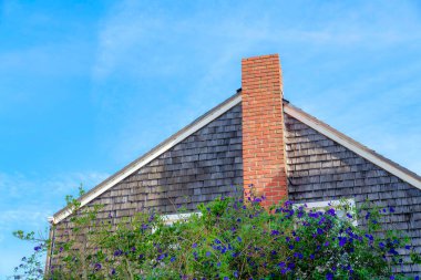 Flowering plants outside a house with wood shingles sidings and chimney with bricks. Home exterior at San Francisco, California in a low angle view against the sky.