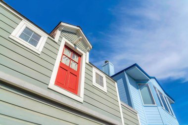 Houses with gray and blue wood vinyl sidings in San Francisco, California. There is a house on the left with red door on its second floor without railings or stairs near the blue house.